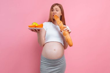 Bir tabak meyve ve pembe arka planda bir somun ekmek ile hamile kadın