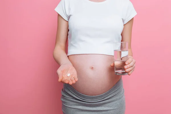 Έγκυος γυναίκα που κρατά ένα ποτήρι νερό και χάπια, βιταμίνες για την εγκυμοσύνη, η μέλλουσα μητέρα περιμένει ένα μωρό — Φωτογραφία Αρχείου
