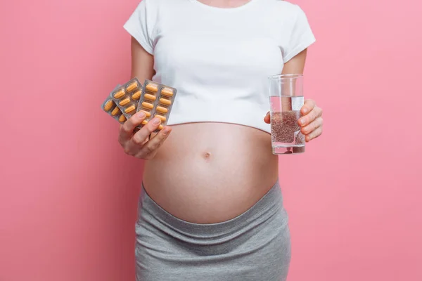 一个年轻的孕妇的手拿着水泡包的药片。怀孕期间接受维生素。在粉红色背景上 — 图库照片