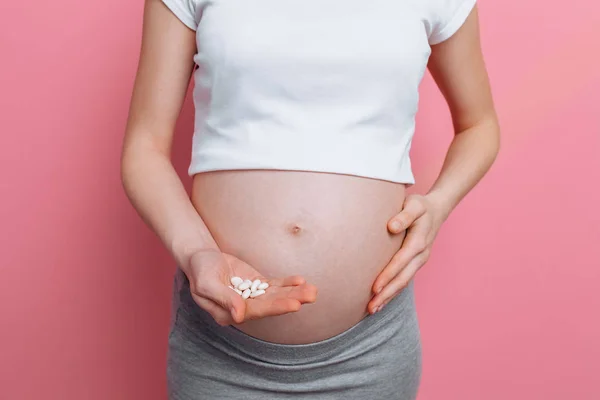 Estomac d'une femme enceinte tenant des pilules rondes blanches pour les soins de santé, gros plan du corps humain sans visage — Photo