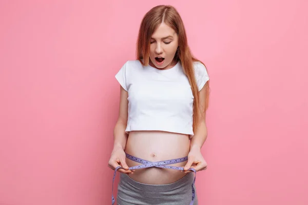 Wstrząśnięty Kobieta w ciąży mierzy jej duży brzuch za pomocą miary taśmy — Zdjęcie stockowe