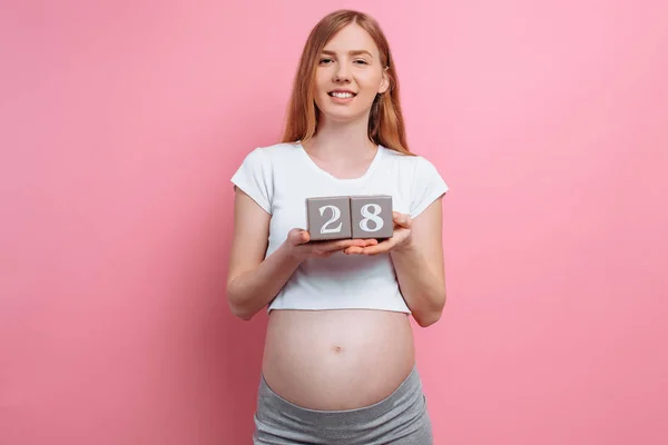 Femme enceinte tenant des cubes de bois près du ventre, grossesse sur un fond rose — Photo