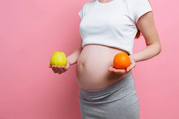 Pregnant woman holding a green apple and an orange near the belly. The concept of pregnancy, maternity, proper nutrition — Stock Photo, Image