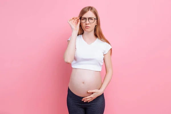 Fille enceinte dans un t-shirt avec des lunettes pour les malvoyants. sur fond rose — Photo