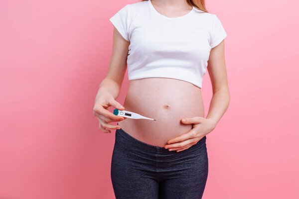 Pregnant woman with a thermometer in her hands, on a pink background