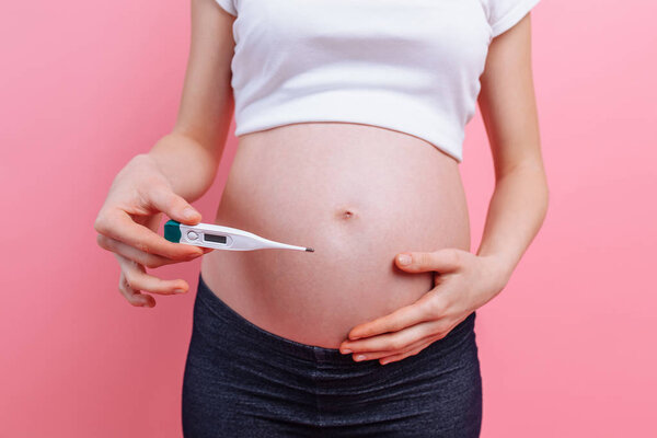 Pregnant woman with a thermometer in her hands, on a pink background