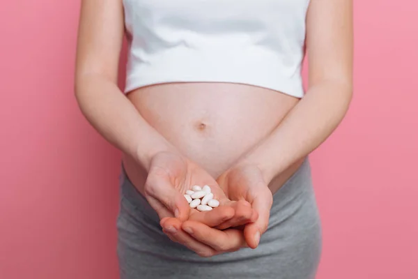 Στομάχι μιας εγκύου γυναίκα κρατώντας στρογγυλά λευκά χάπια για την υγειονομική περίθαλψη, κοντινό-up του ανθρώπινου σώματος χωρίς πρόσωπο — Φωτογραφία Αρχείου