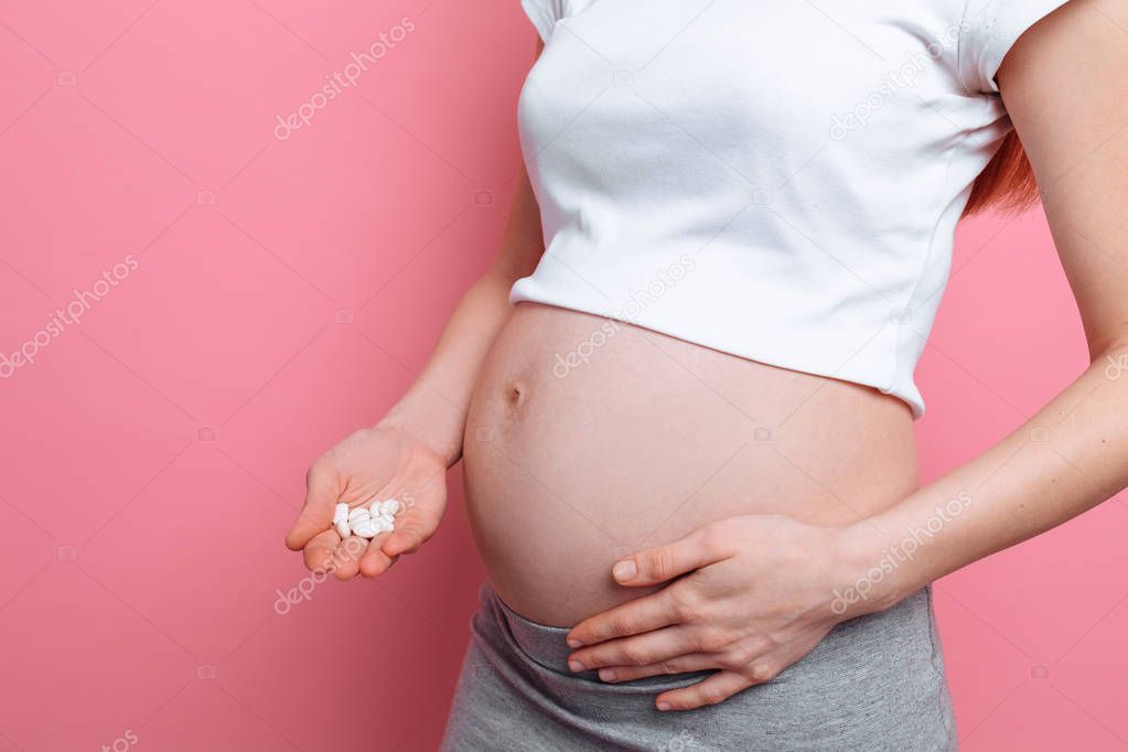Stomach of a pregnant woman holding round white pills for health care, close-up of the human body without a face