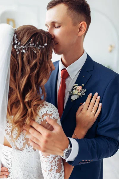 Hermosa novia en vestido blanco y novio en traje, posando en el interior del estudio blanco, boda — Foto de Stock