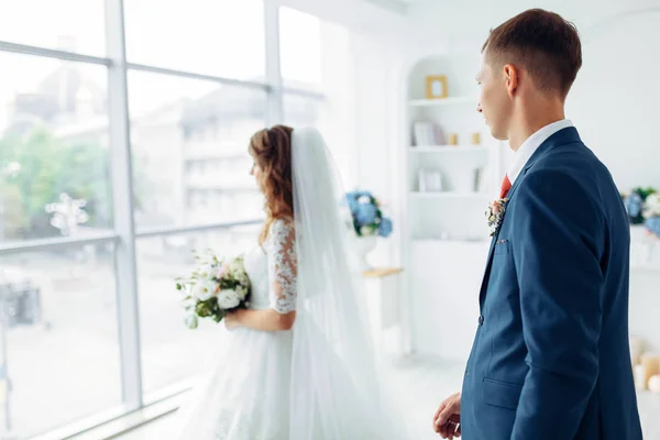Vacker brud i vit klänning och brudgummen i kostym, poserar i vit Studio inredning, bröllop — Stockfoto