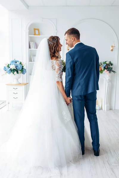 Bela noiva em vestido branco e noivo em terno, posando em interior estúdio branco, casamento — Fotografia de Stock