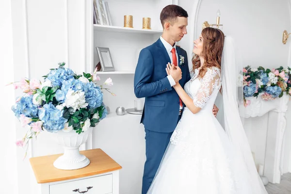 Όμορφη νύφη σε λευκό φόρεμα και ο γαμπρός στο κοστούμι, ποζάρει σε λευκό στούντιο εσωτερικό, γάμος — Φωτογραφία Αρχείου