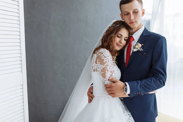 Bela noiva em vestido branco e noivo em terno, posando em interior estúdio branco, casamento — Fotografia de Stock