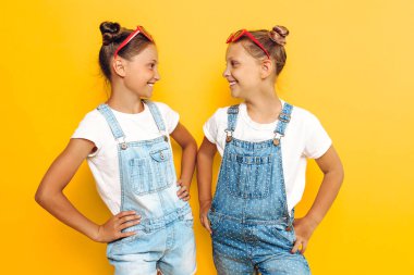 İki genç kız, arkadaşlar, sarı bir arka plan üzerinde poz ve lo