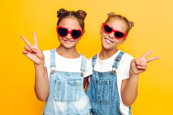 Deux adolescentes, copines élégantes dans des lunettes de soleil posant sur un fond jaune — Photo