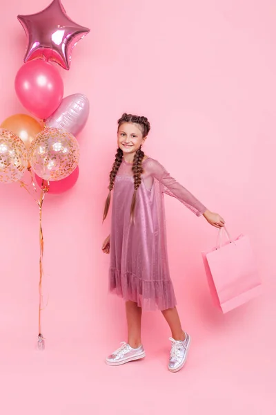 Chica feliz con globos y bolsas de compras posando sobre una espalda rosa — Foto de Stock