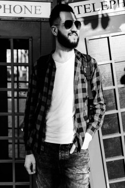 sakallı hipster, kırmızı telefon kulübesinin karşısında şehirde poz veren beyaz tişörtlü ve güneş gözlüğü takan bir adam.