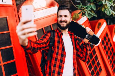 güneş gözlüğü sakallı adam, kaykay ile ekose gömlek giymiş bir hipster, bir akıllı telefonda selfie alır