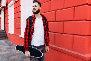 sakallı adam, bir hipster elinde bir kaykay ile şehirde dolaşıyor.