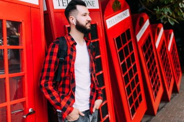 sakallı hipster, beyaz tişörtlü bir adam ve ekose gömlekli, kırmızı telefon kulübesinin karşısındaki şehirde poz veren bir adam.