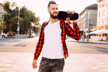 sakallı adam, bir hipster elinde bir kaykay ile şehirde dolaşıyor.