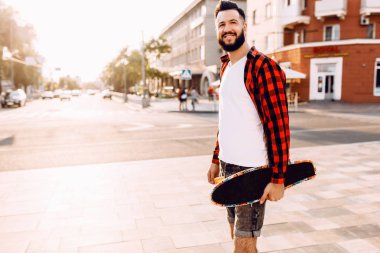 sakallı adam, bir hipster elinde bir kaykay ile şehirde dolaşıyor.