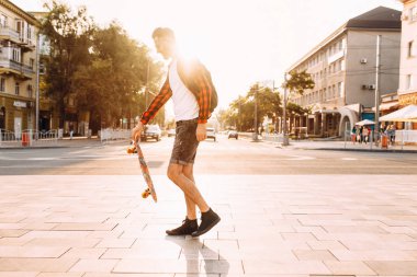 Kablosuz kulaklık bir sakallı şık adam şehir etrafında bir kaykay ile yürüyor