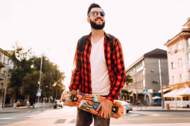 güneş gözlüğü sakallı adam, gün batımında bir kaykay ile yürür.