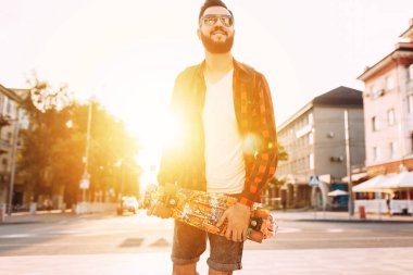 güneş gözlüğü sakallı adam, gün batımında bir kaykay ile yürür.