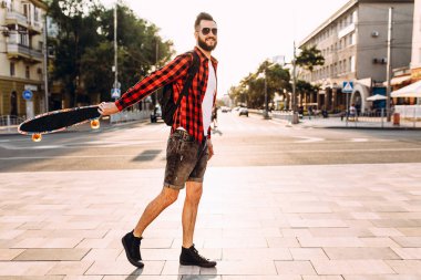 güneş gözlüğü sakallı adam, gün batımında bir kaykay ile yürür.