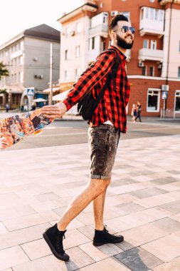 güneş gözlüğü sakallı adam, gün batımında bir kaykay ile yürür.