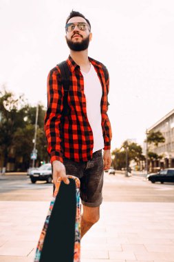 güneş gözlüğü sakallı adam, gün batımında bir kaykay ile yürür.