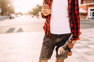 sakallı adam, elinde bir kaykay ve akıllı telefon ile şehirde dolaşıyor