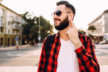 Kablosuz kulaklık sakallı şık adam şehirde dolaşıyor ve müzik dinliyor.