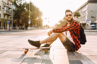 kablosuz kulaklık bir sakallı adam bir kaykay ile bir parkta oturur