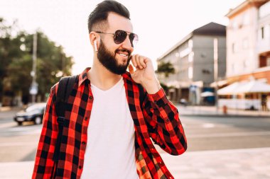 Kablosuz kulaklık sakallı şık adam şehirde dolaşıyor ve müzik dinliyor.