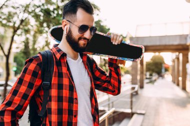 Kablosuz kulaklık bir sakallı şık adam şehir etrafında bir kaykay ile yürüyor