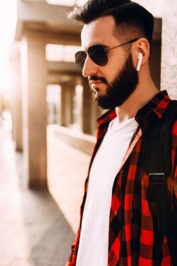 Kablosuz kulaklık sakallı şık adam şehirde bir binanın yakınında poz