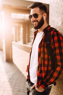 Kablosuz kulaklık sakallı şık adam şehirde bir binanın yakınında poz