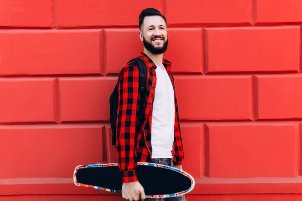 Kille med skägg på en bakgrund av en tegel tom vägg med en skateboard — Stockfoto