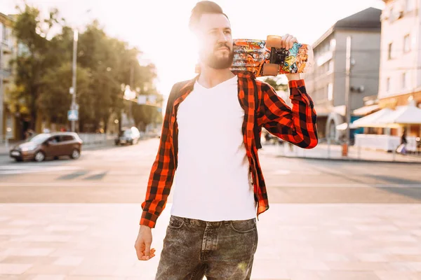 sakallı adam, bir hipster elinde bir kaykay ile şehirde dolaşıyor.