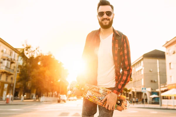 Kablosuz kulaklık bir sakallı şık adam şehir etrafında bir kaykay ile yürüyor