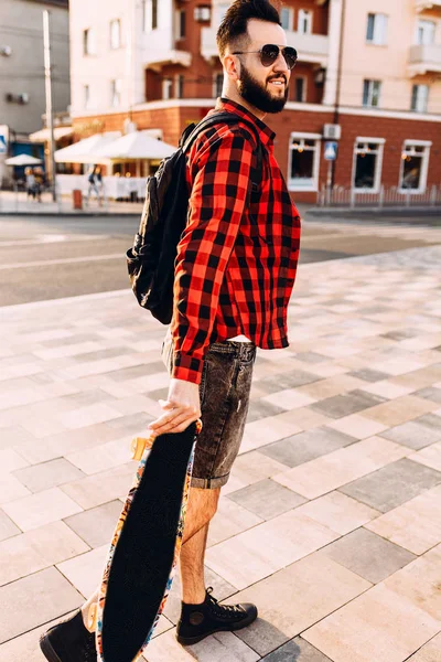 güneş gözlüğü sakallı adam, gün batımında bir kaykay ile yürür.