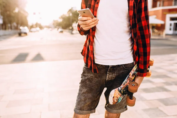 sakallı adam, elinde bir kaykay ve akıllı telefon ile şehirde dolaşıyor