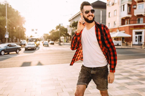 Stylish guy with a beard in wireless headphones walks around the city and listens to music. — Stock Photo, Image