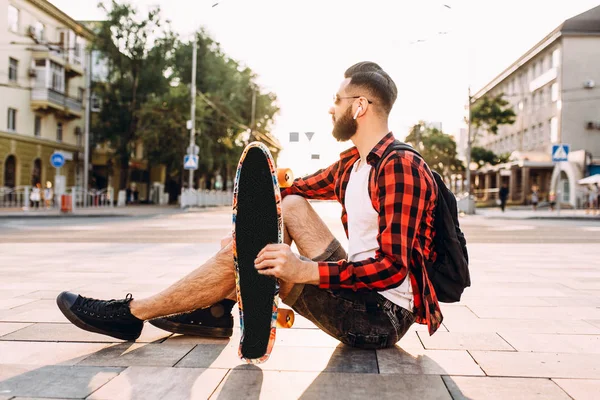 kablosuz kulaklık bir sakallı adam bir kaykay ile bir parkta oturur