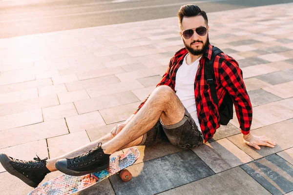 Kablosuz kulaklık bir sakallı şık adam şehir etrafında bir kaykay ile yürüyor