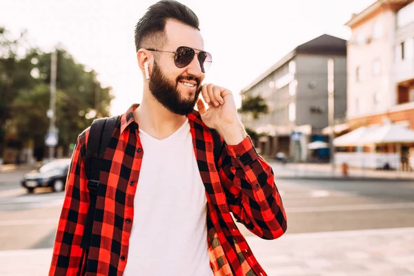 Kablosuz kulaklık sakallı şık adam şehirde dolaşıyor ve müzik dinliyor.