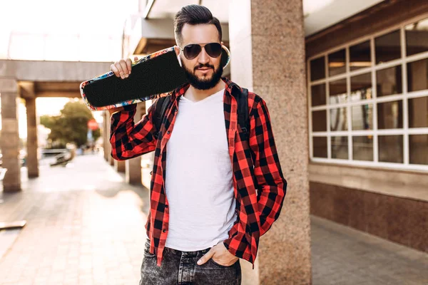 Kablosuz kulaklık bir sakallı şık adam şehir etrafında bir kaykay ile yürüyor