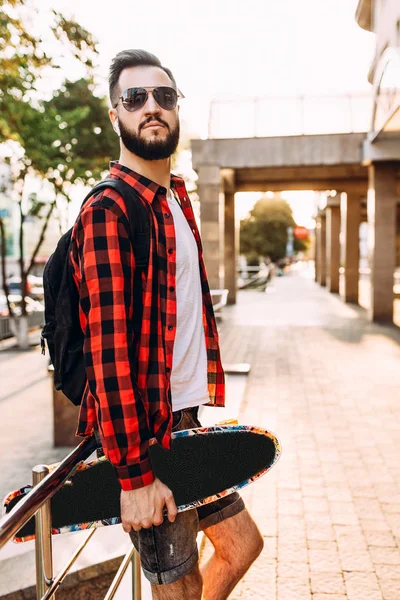 Kablosuz kulaklık bir sakallı şık adam şehir etrafında bir kaykay ile yürüyor